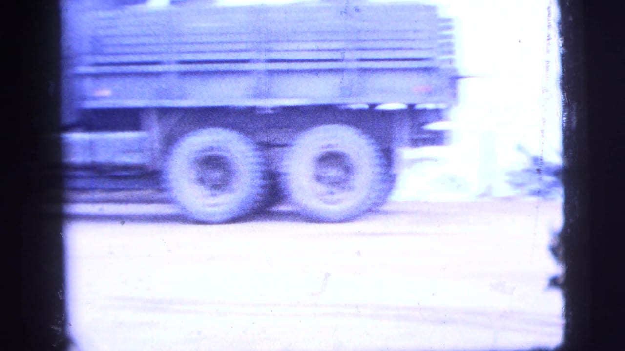 1956 New York City 8mm frame showing a military-style truck moving past an industrial roadside in soft blue-tinted light.