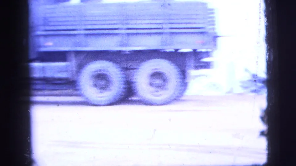 1956 New York City 8mm frame showing a military-style truck moving past an industrial roadside in soft blue-tinted light.
