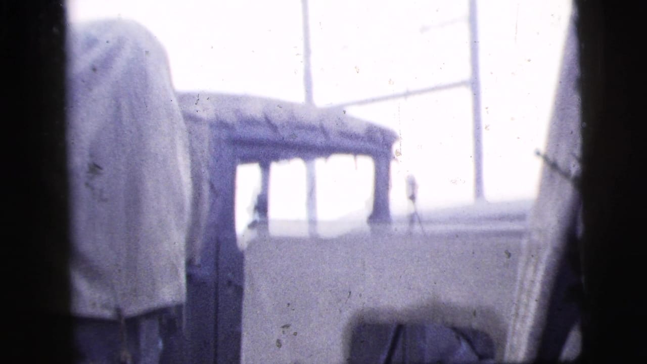 Soft 8mm frame from 1956 New York City showing a small light-colored vehicle or structure near large industrial windows.