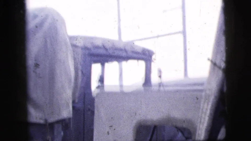 Soft 8mm frame from 1956 New York City showing a small light-colored vehicle or structure near large industrial windows.