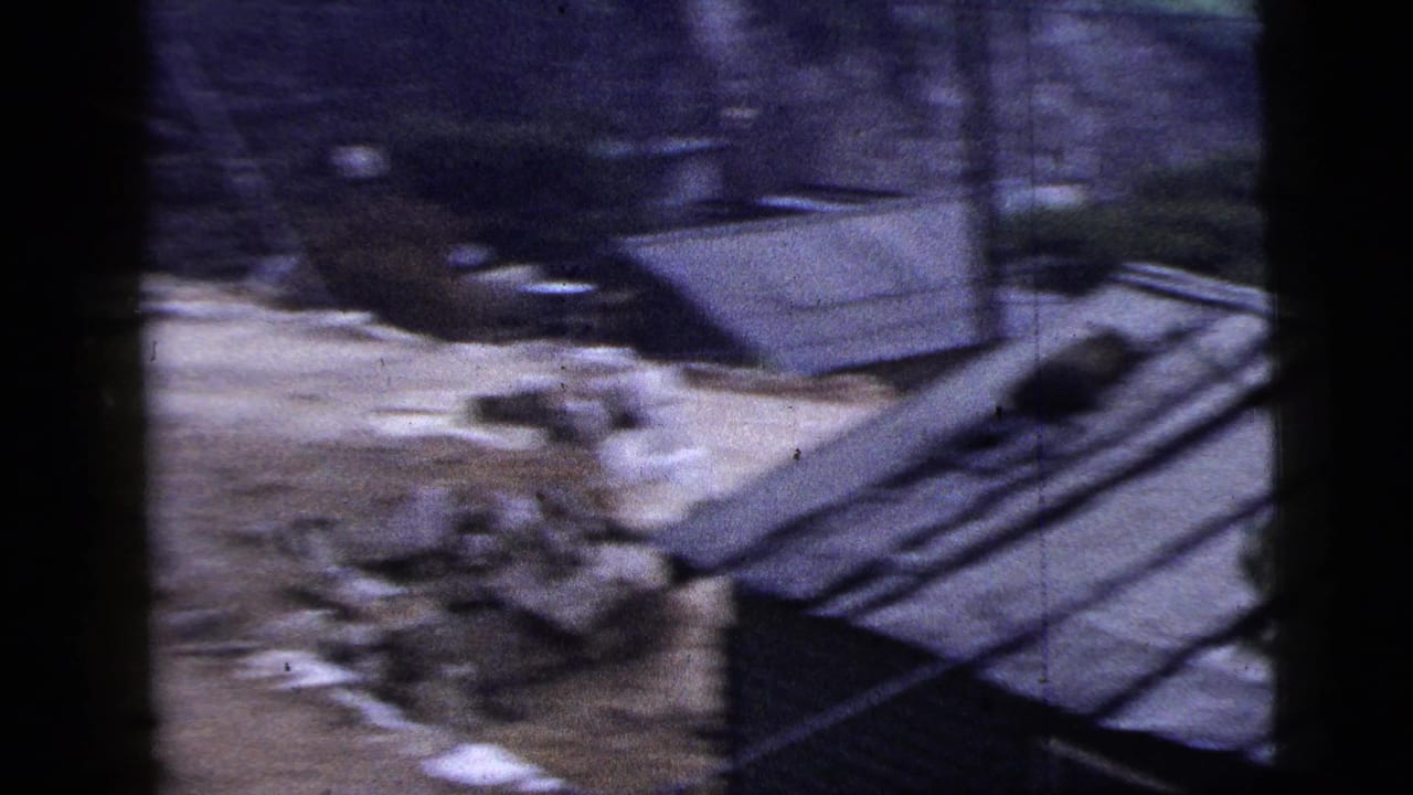 Handheld 1956 New York City 8mm frame showing rubble, exposed earth, corrugated siding, and dark vertical foreground shapes.