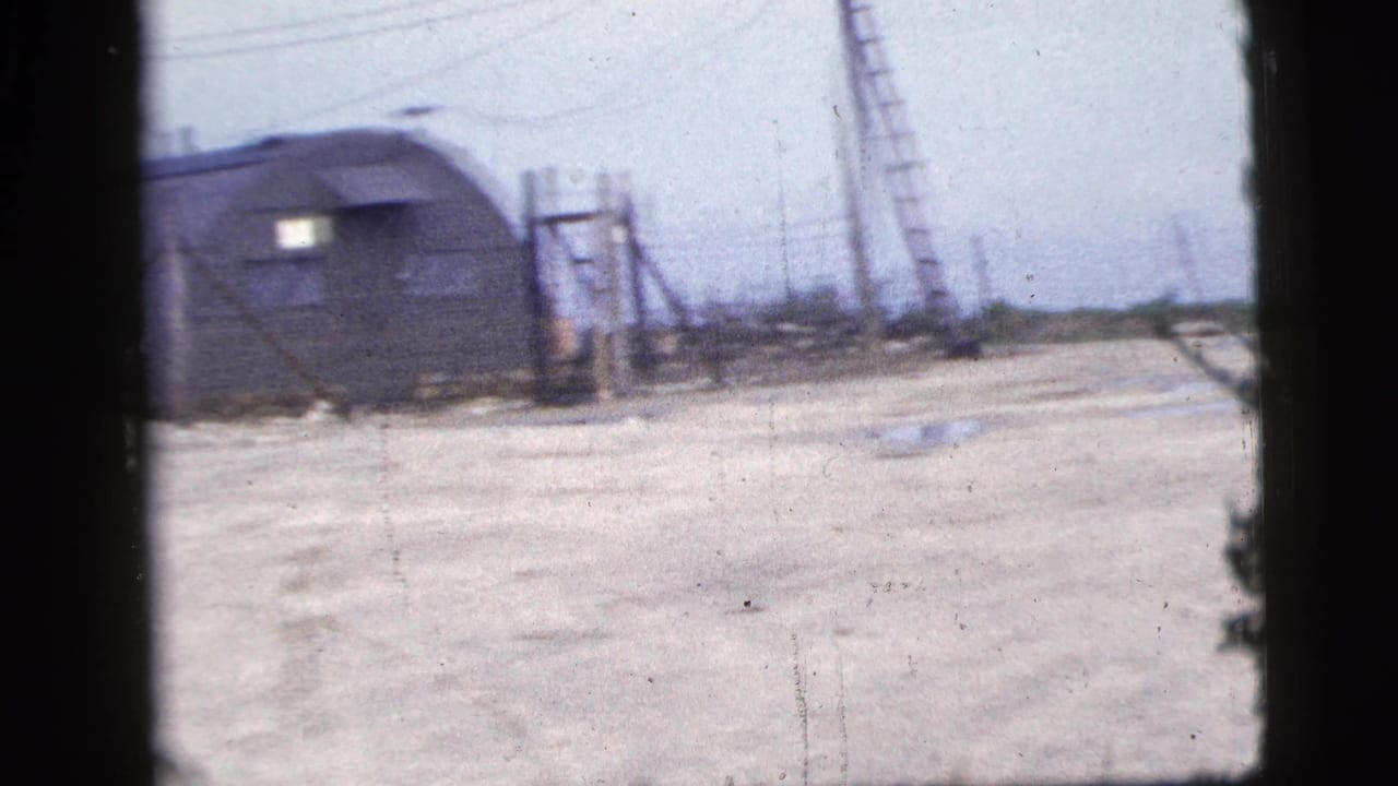 1956 New York City 8mm view of a Quonset-style hut beside a wide concrete yard with utility poles and leaning ladders.