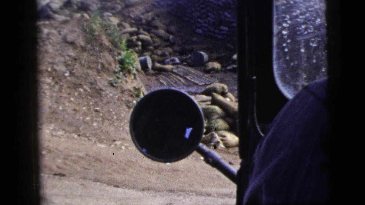 Vehicle side mirror and window frame beside a stone-lined roadside work area.