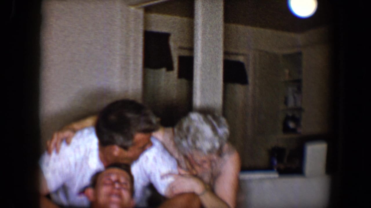 Two adults lean over a laughing man on a sofa in a private living room.