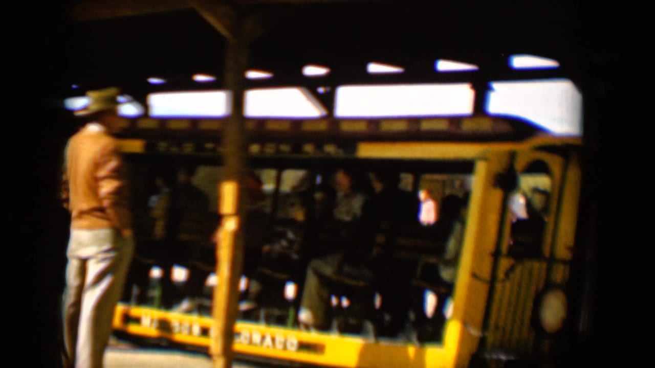 A man in a hat stands beside the Old Tucson R.R. trolley as passengers remain seated inside the open-sided car.