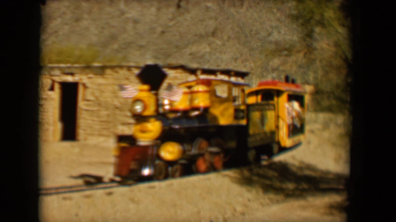 A yellow and red steam-style train passes a stone-walled rustic structure in Tucson, 1958.