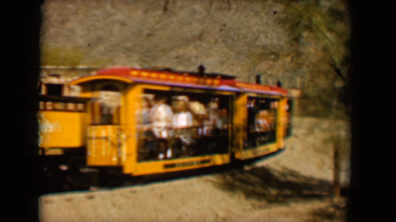 Open yellow train cars with visible passengers pass through the rustic Tucson attraction setting, 1958.