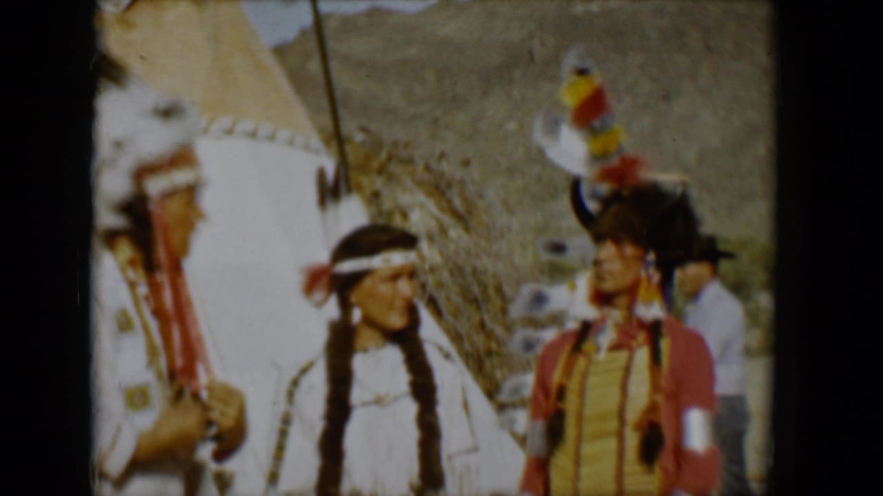 Two adults face each other beside a tipi while another figure is partly visible at the edge.