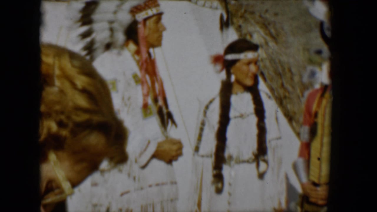 A close passerby partially blocks people in regalia standing beside a teepee.