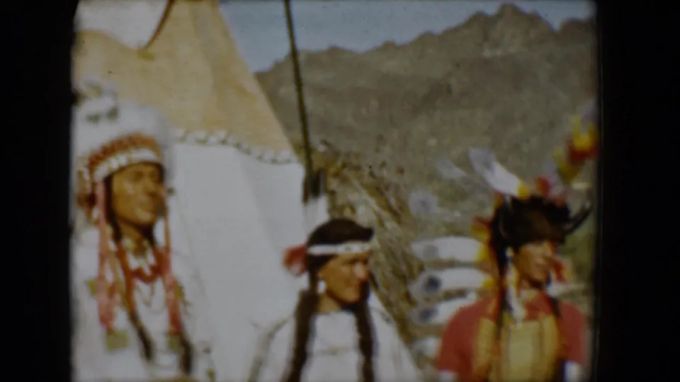 1958 Tucson frame showing three visible figures in feathered and fringed regalia beside teepee canvas, with a mountainous desert backdrop.