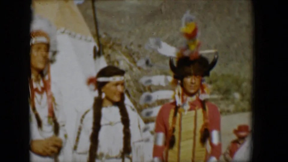 Soft 8mm frame from Tucson in 1958 with three people in regalia near a teepee, including one partly cropped figure at left.