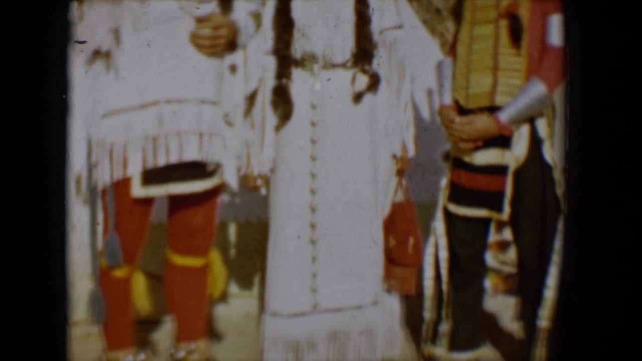 Cropped 1958 Tucson frame showing people in regalia, including white fringed clothing, red leggings, and a figure at the right edge.
