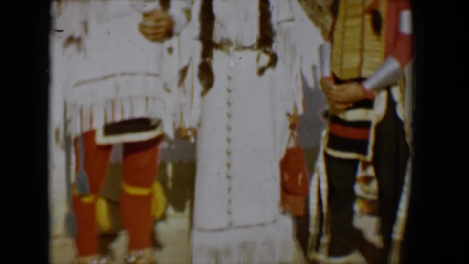 Cropped 1958 Tucson frame showing people in regalia, including white fringed clothing, red leggings, and a figure at the right edge.