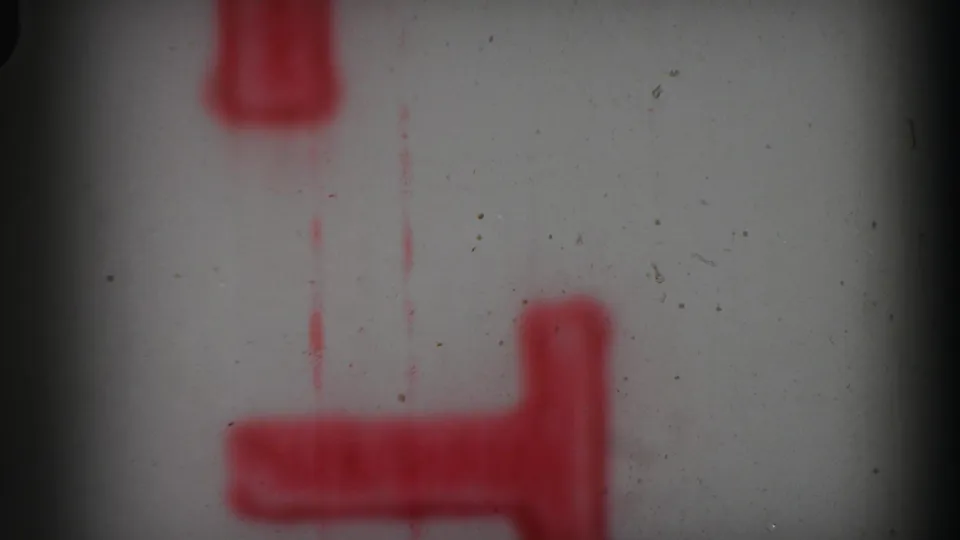 1969 8mm frame showing partial red leader-like markings on a pale surface, with visible dust and dark gate edges.