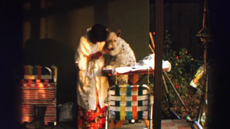 In 1969 Lake Tahoe home-movie footage, a woman in a white robe tends a fluffy dog on a backyard table.