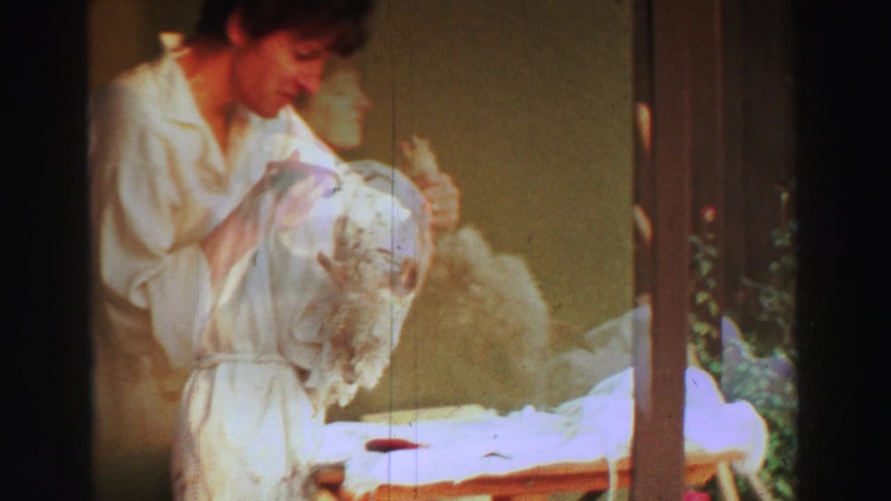 Woman in a white robe trims a fluffy dog on a covered backyard table.