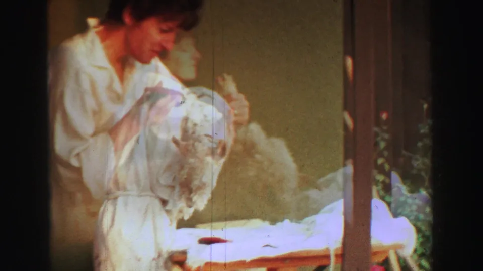In Lake Tahoe 1969 home-movie footage, a woman in a white robe bends over a fluffy dog on a backyard grooming table.