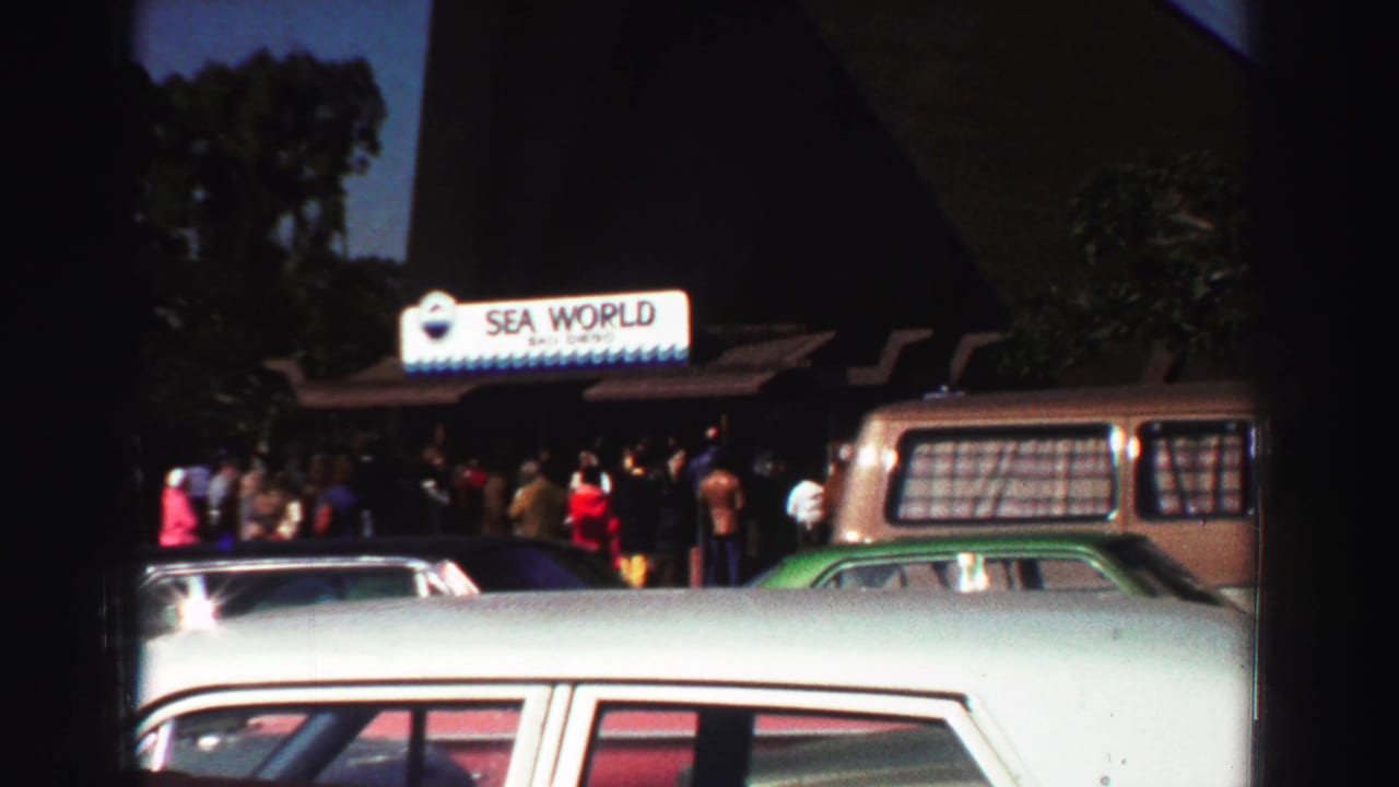 Sea World entrance sign with visitors and parked cars in the foreground.