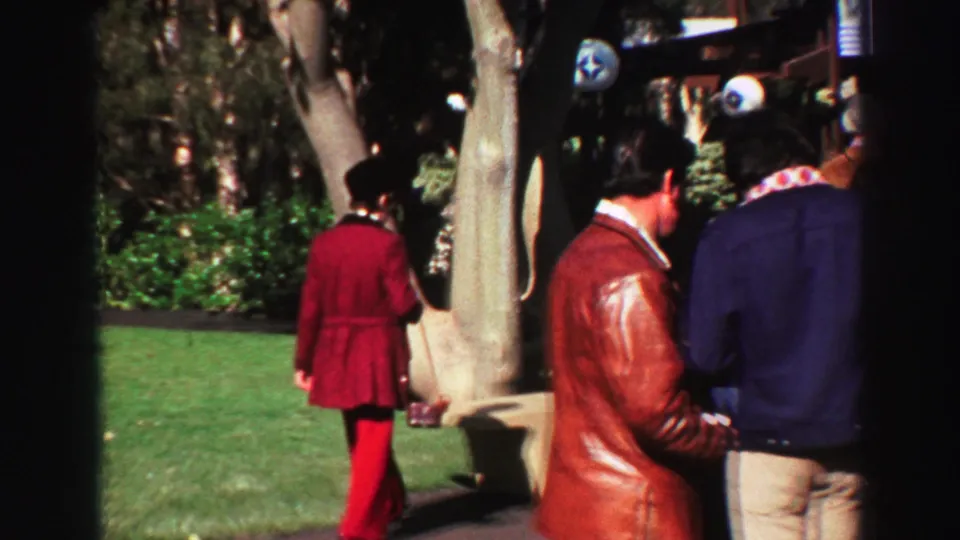 1969 Lake Tahoe frame showing adults in period jackets and hats walking through a landscaped lakeside park area.