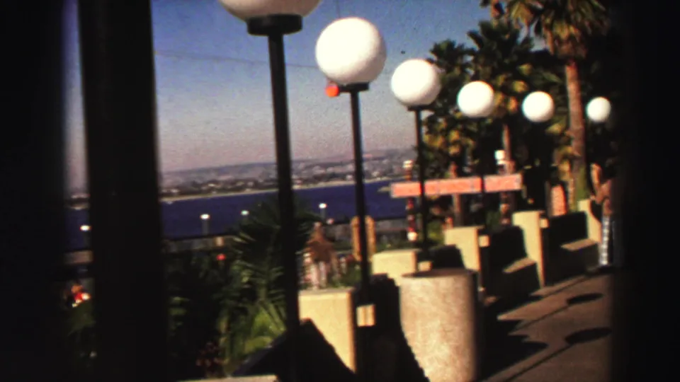 1969 Lake Tahoe home-movie frame showing a resort walkway lined with globe lamps and palm plantings above the lake.