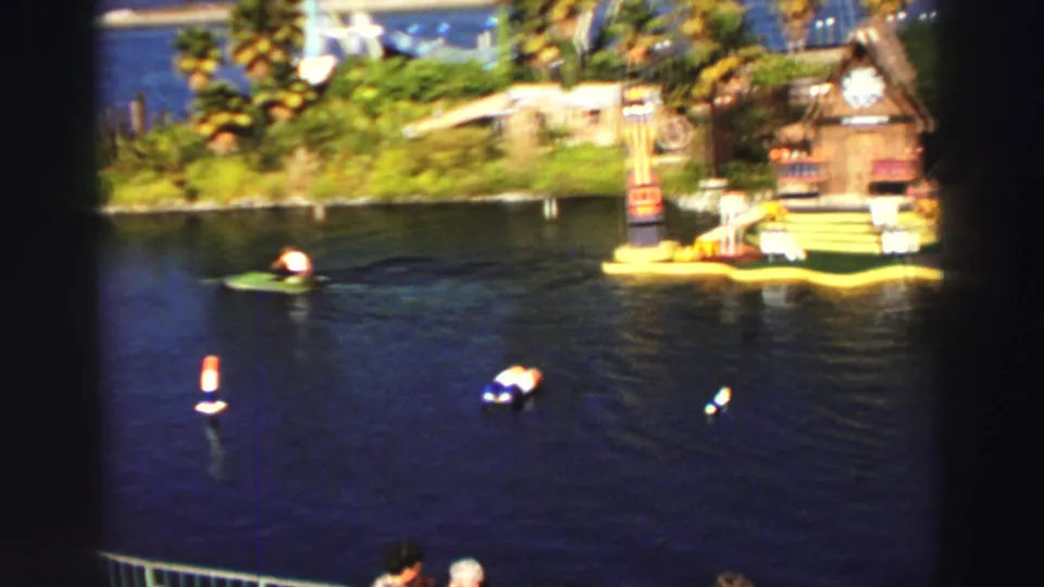 Wide 1969 Lake Tahoe home-movie view with the small green boat, scattered buoys, dark water, and a themed floating attraction near shore.
