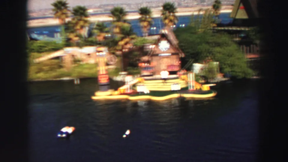 1969 Lake Tahoe frame showing a tropical-themed floating attraction with a wooden hut, palm-like plants, buoys, and open lake water.