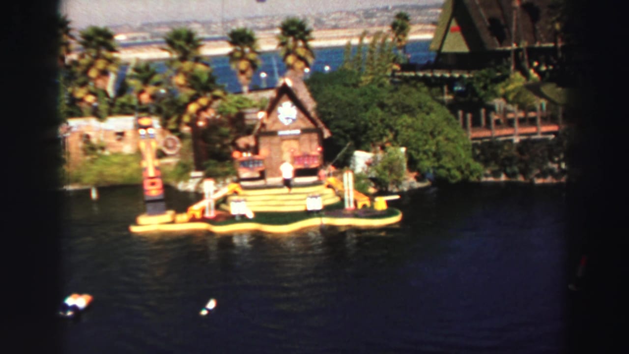 Floating miniature golf island with wooden lodge, colorful obstacles, palm trees, lake water, and small boats.