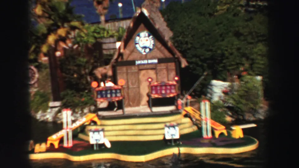 Close 1969 Lake Tahoe frame of the floating attraction's Locker Room lodge, steps, benches, oversized pins, and lake edge.