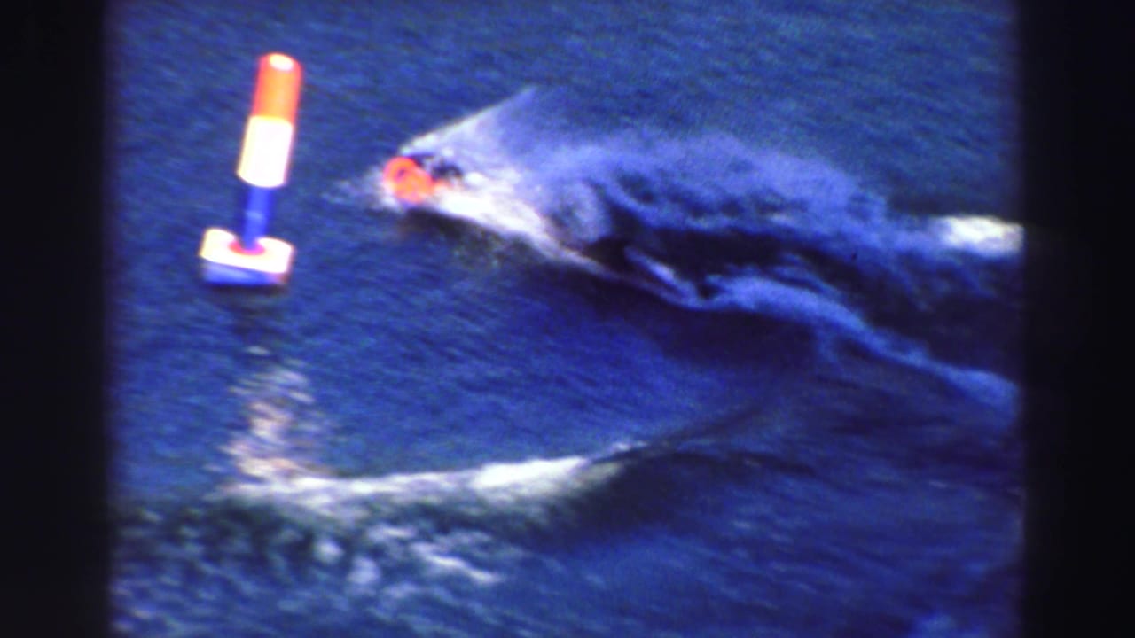 Water skier in a red cap passes a floating buoy on dark blue water.