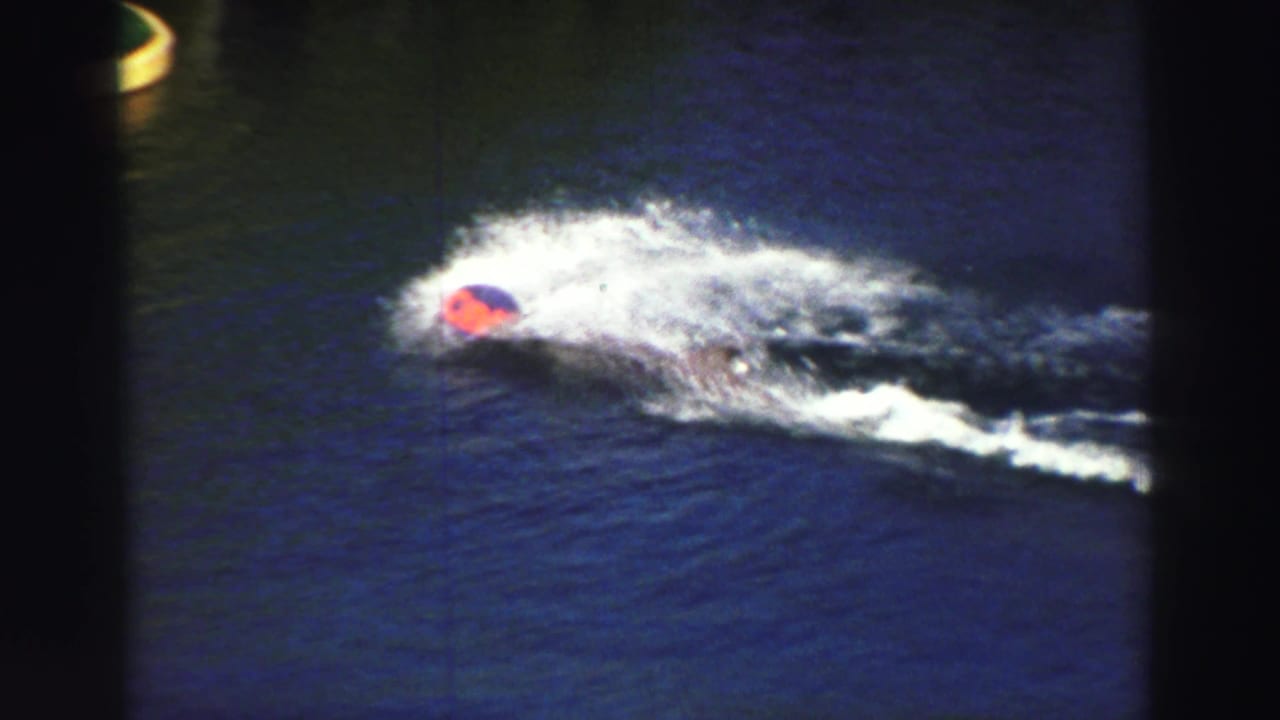 Lake Tahoe 1969 frame of a water skier in a red cap partly obscured by white spray on blue water.