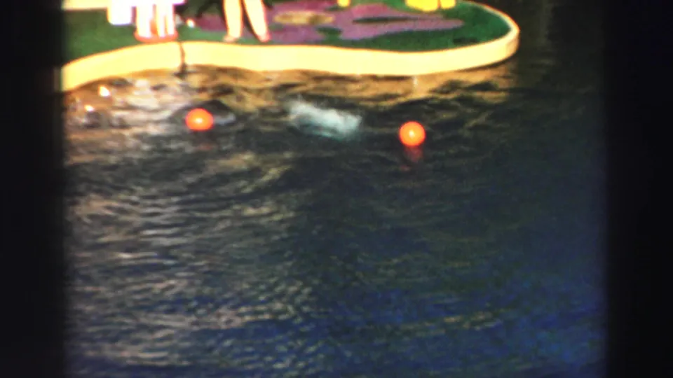 1969 Lake Tahoe dolphin-show frame with orange balls floating in the pool below a cropped artificial island platform.