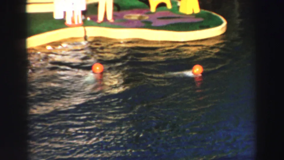 1969 Lake Tahoe home-movie frame showing two orange balls in the dolphin pool near the colorful stage edge.