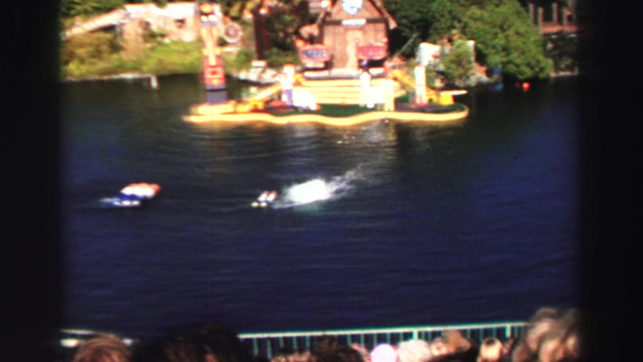 Wide view of lake water, floating props, spectators, and a show platform in the background.