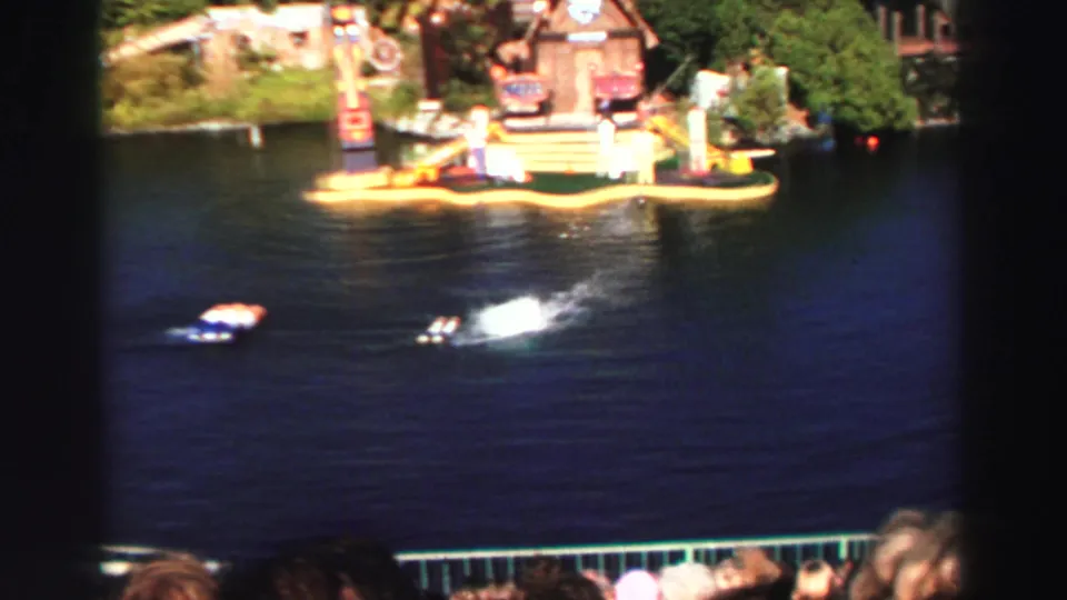 Wide Lake Tahoe water-show view with small floating props crossing the lake and spectators visible along the lower edge.