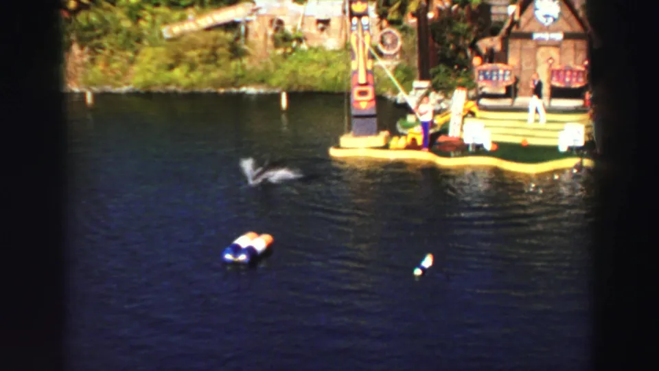 1969 Lake Tahoe water-show frame showing a dolphin leaping near a performer and floating stage props.