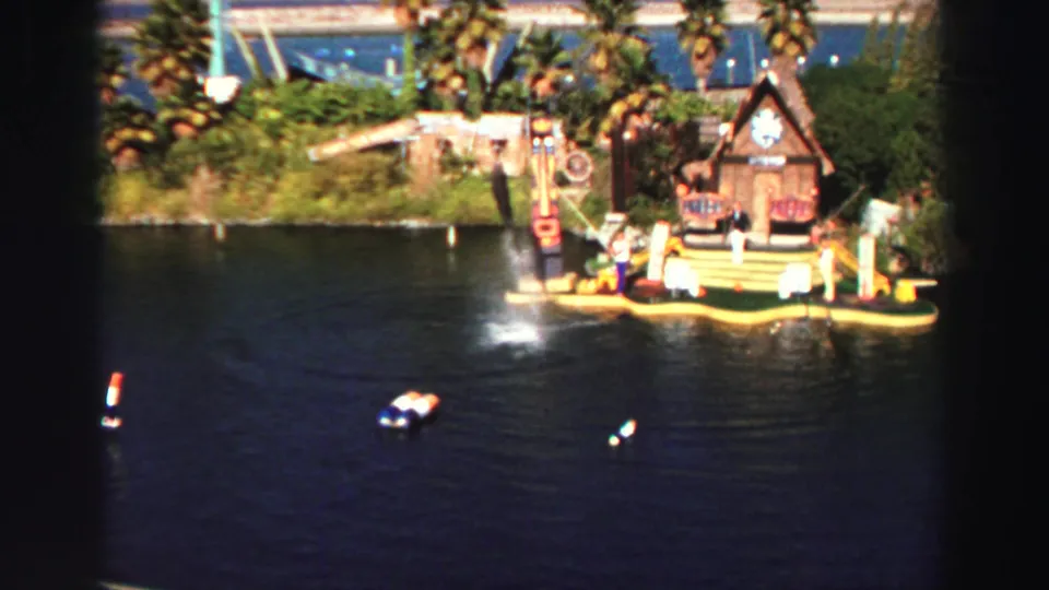 1969 Lake Tahoe water-show frame showing a dolphin beginning to leap beside a colorful floating platform.