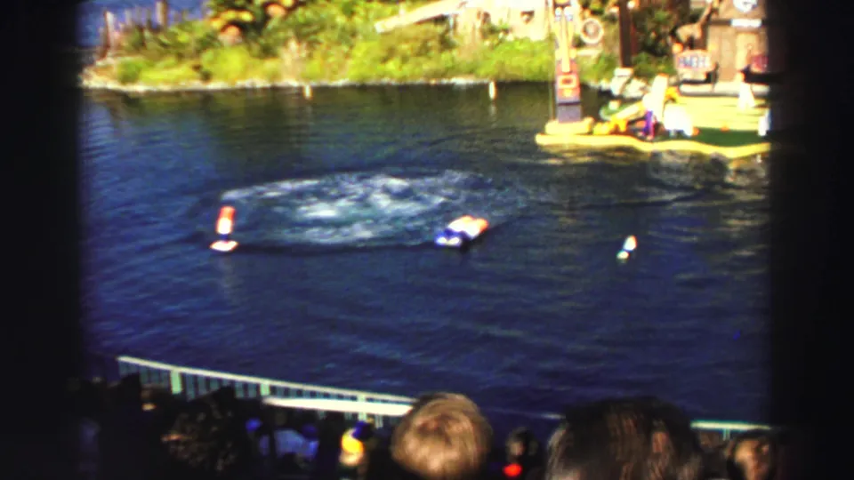1969 Lake Tahoe home-movie frame showing a water arena, floating markers, shoreline set pieces, and audience heads in the foreground.
