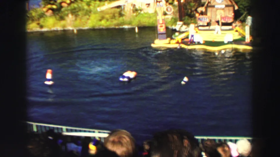 Visitor-shot 1969 Lake Tahoe frame with the aquatic show area, small buoys, trainer platform, greenery, and spectators in front.