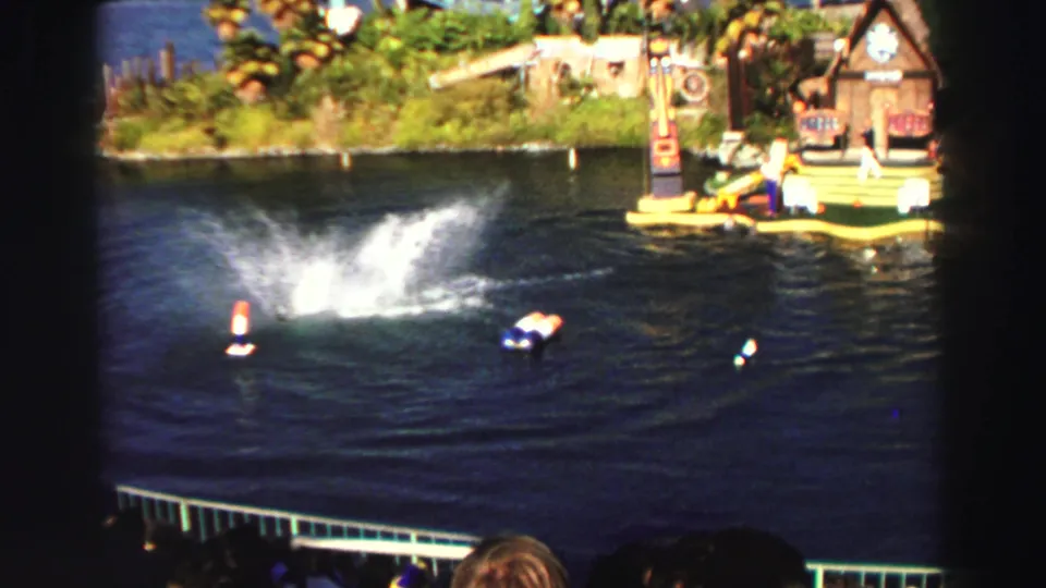 1969 Lake Tahoe home-movie frame showing the splash after a dolphin backflip in an outdoor water arena before spectators.