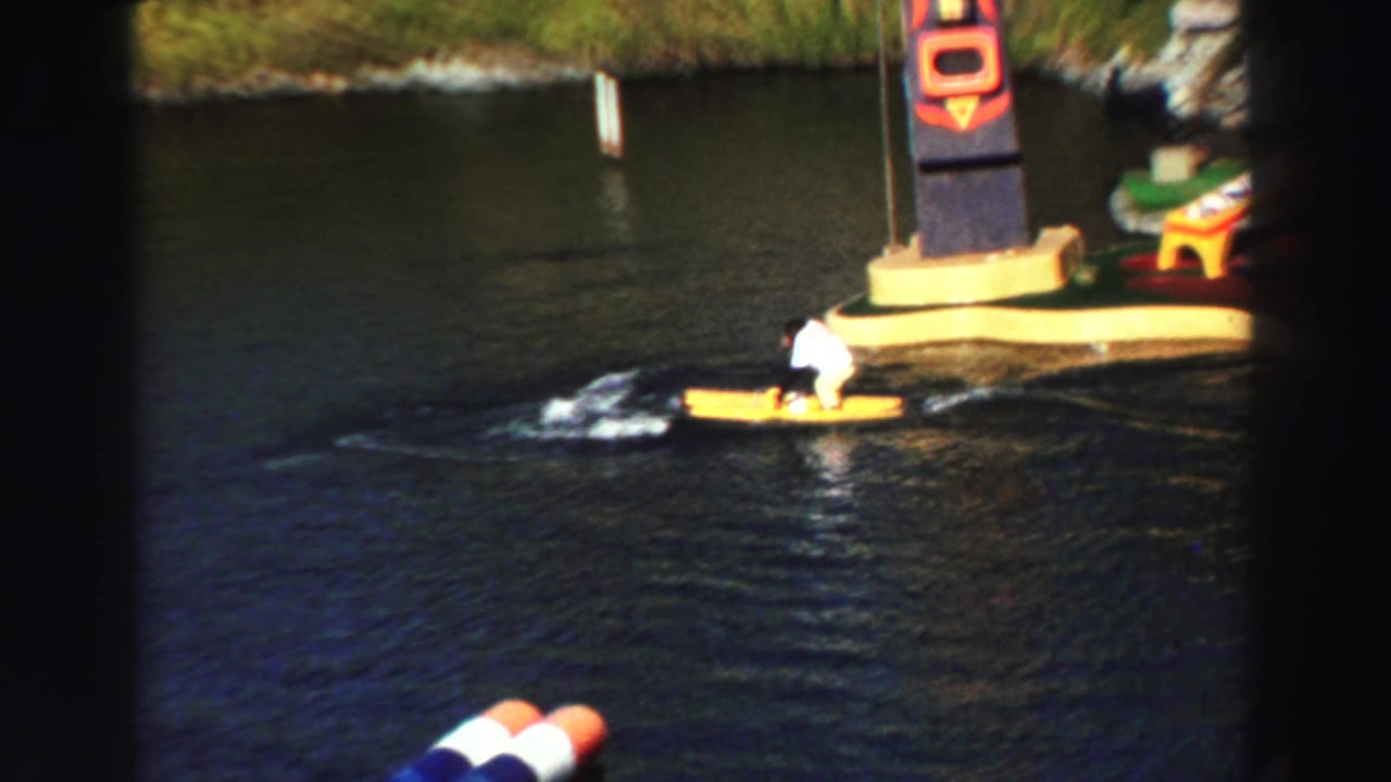 Monkey in a white outfit rides a yellow watercraft across a dark pond near a painted column.