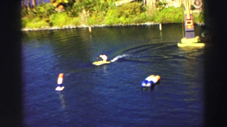 1969 Lake Tahoe home-movie frame showing the costumed monkey maneuvering the yellow craft around floating course obstacles.