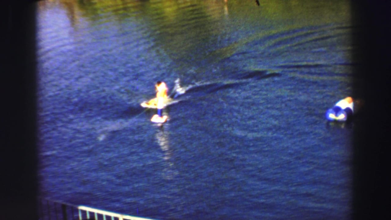 Distant rider on a yellow board is towed across blue lake water near a small buoy.