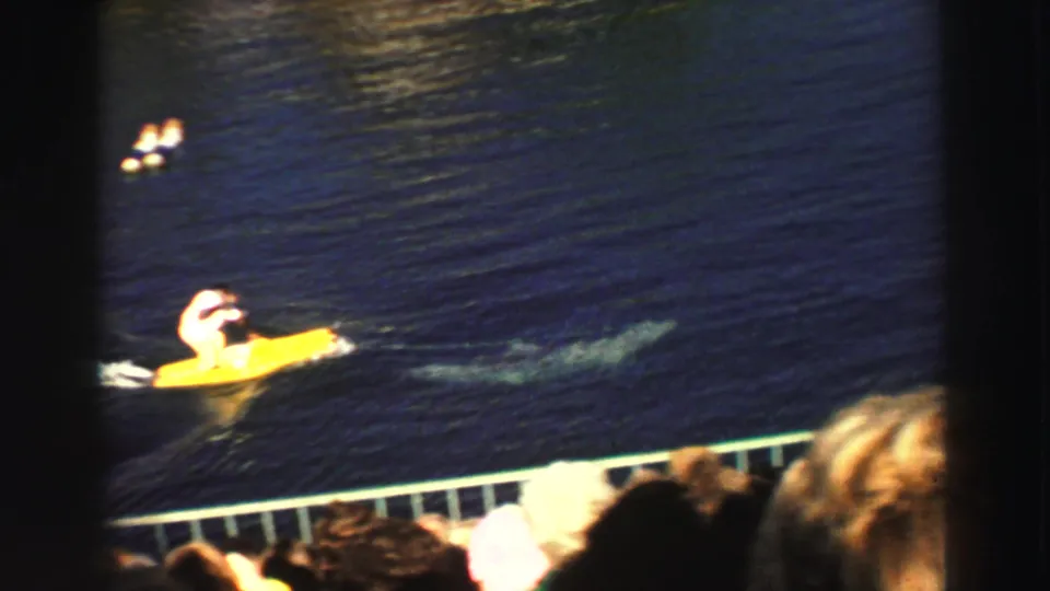 1969 Lake Tahoe home-movie frame showing the yellow board rider passing in front of spectators during an aquatic show or display.