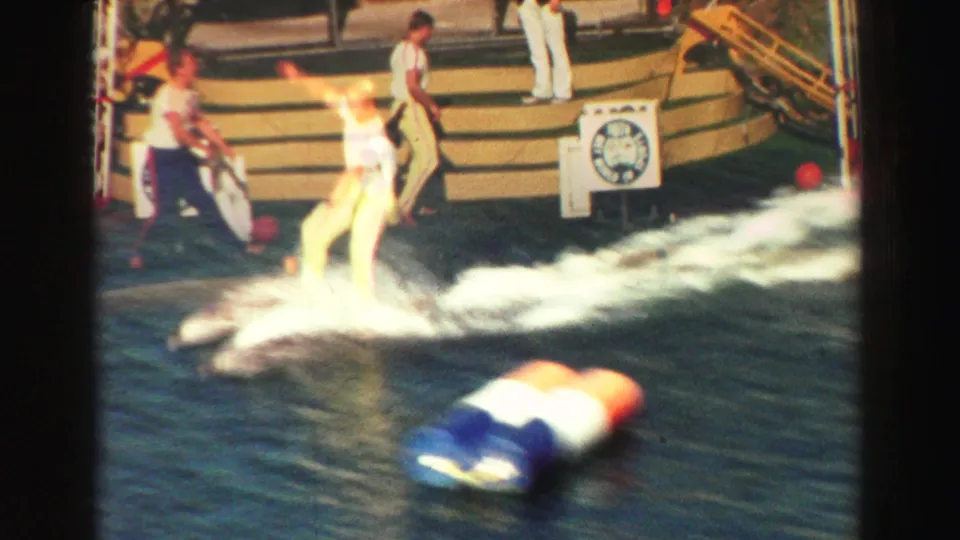 1969 Lake Tahoe frame showing staff or spectators near stepped seating as a dolphin splashes close to the water edge.