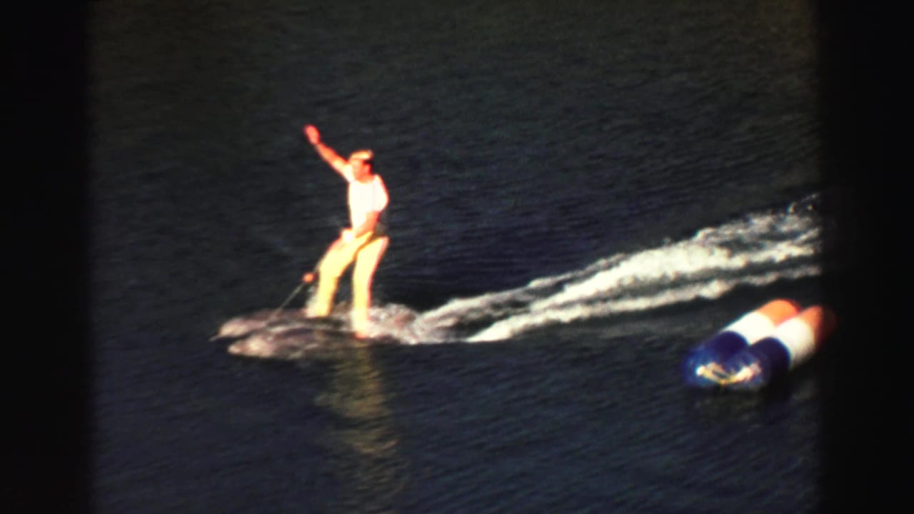 Performer balancing on the water as a wake trails behind, with a buoy nearby.