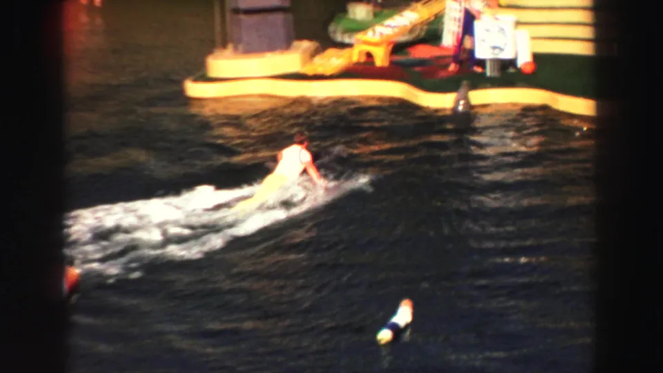 1969 Lake Tahoe frame showing a performer low on the water near floating markers and a brightly painted platform at the edge of the show area.