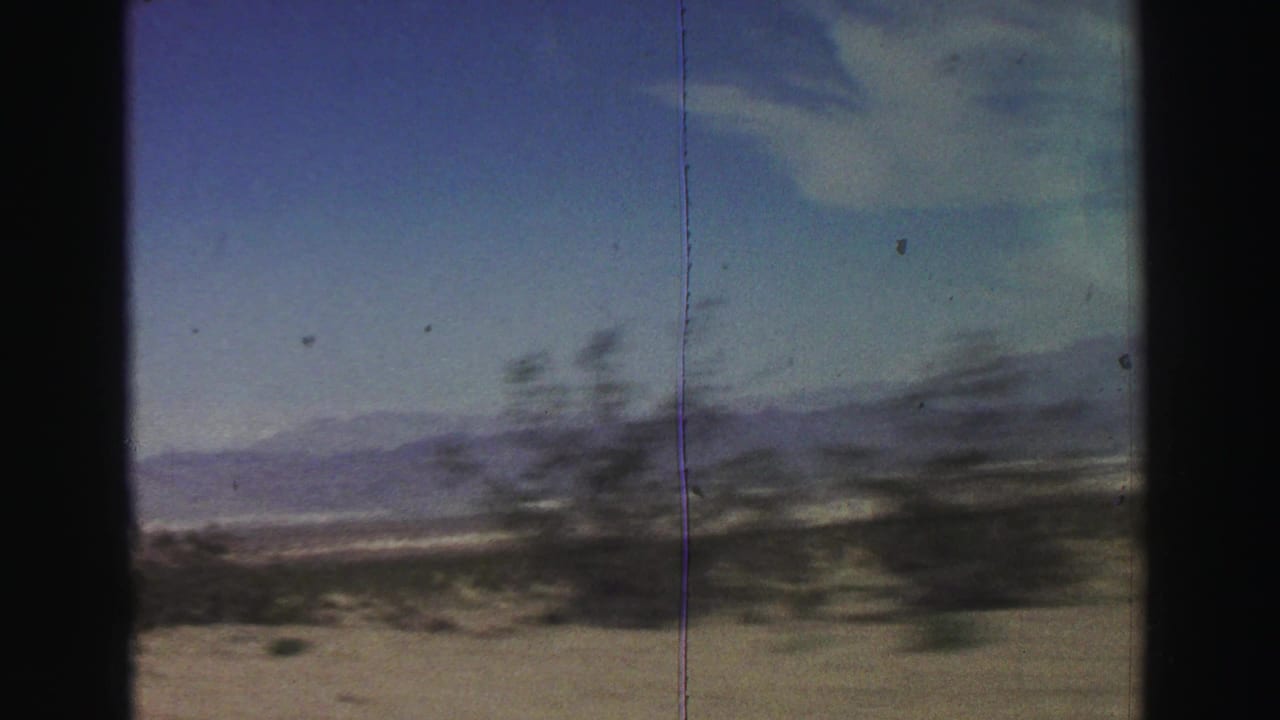 Desert brush blurs past with distant mountains under a blue sky.