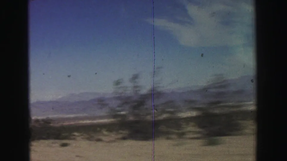 1969 8mm road-view footage near Lake Tahoe shows desert brush, sandy ground, and distant mountain ridges through a moving vehicle window.
