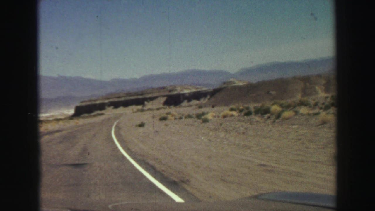Curving desert highway seen from a moving vehicle with mountains in the distance.
