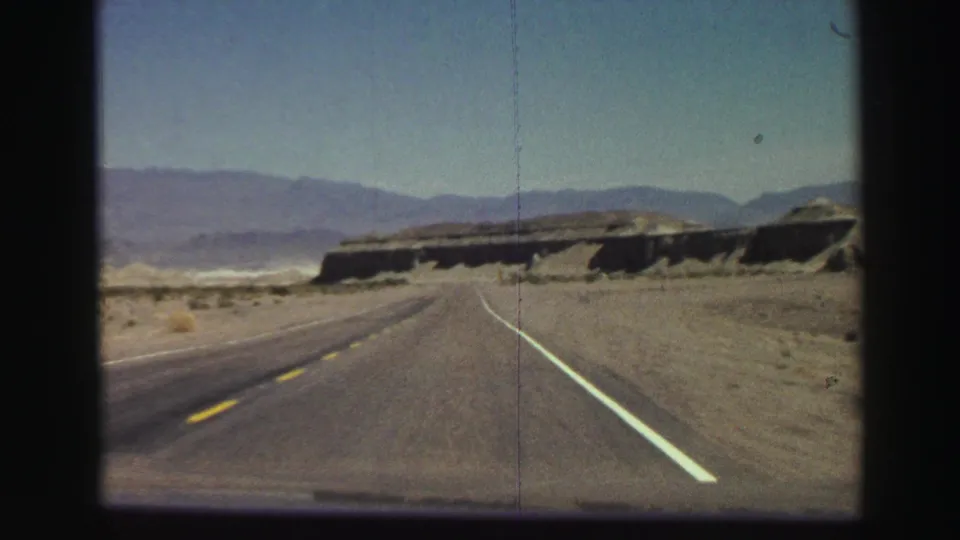 Forward-facing 8mm road view on a highway in arid California mountain terrain, with no people or signs visible.